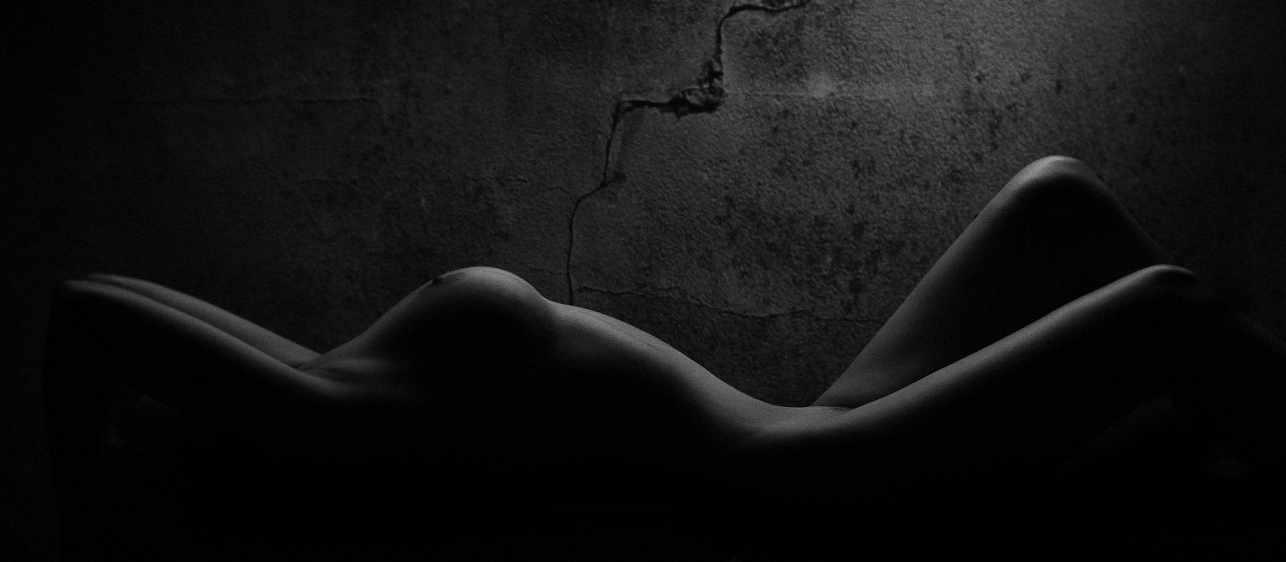 Nude woman in dark lite room, breasts highlighted by the light
